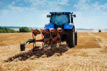A plow attached to a blue tractor, arable land, field preparation - obrazy, fototapety, plakaty