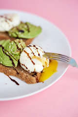 Breakfast toast with poached egg and avocado on the white plate. Pink background