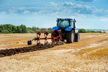 blue tractor pulls plow, arable land, field preparation