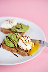 Breakfast toast with poached egg and avocado on the white plate. Pink background
