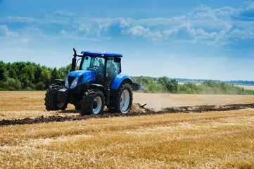 blue new tractor plowed soil on the edge of a field