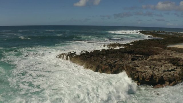 The rough waves of the Pacific Ocean crashing into the rocky coastline of Oahu in the Hawaiian Islands with the camera moving backwards.
