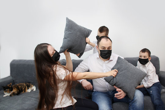 young couple and two children having fun in a room on a gray sofa in black virus masks, red inscription quarantine, concept of the virus epidemic, quarantine