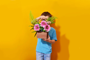 Happy beautiful kid boy holds flower bouquet on the yellow background. Children love nature and...