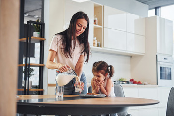 Obraz premium Mother pouring fresh milk into the glass for her little daughter in kitchen