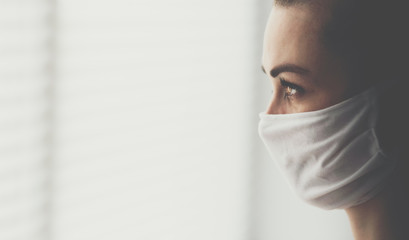 Worried woman in a mask is standing by the window at home - Quarantine time - Coronavirus pandemic...