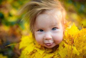 happy little girl laughs and plays outdoors. On the neck there is a necklace of autumn leaves.