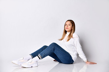 Teenage girl with long hair. Dressed in jeans, sweater, socks and sneakers. She sitting on floor, isolated on white. Close up