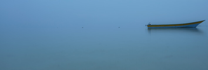 Sole boat in early morning in glassy blue waters and mist in distance with no horizon line  banda sea in Ohoidertawun beach, Maluku, Indonesia