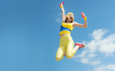 Sporty woman jumping with dumbbells. Funny woman in sportswear on sky background. Dynamic movement....