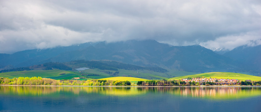 lake in mountains. cloudy day in springtime. rural fields on rolling hills. beautiful scenery of high tatra mountains in dappled light. gorgeous landscape of liptovska mara, slovakia