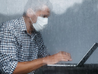 Man working at home during quarantine coronavirus at rainy day. Man wearing face medical mask with...