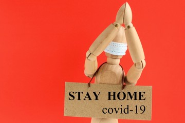 Cardboard sign with text stay home covid-19 hanging on a wooden doll or mannequin in a medical...