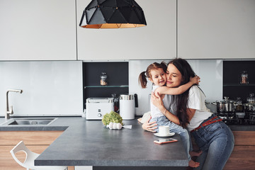 Mother with her little daughter embracing each other indoors in kitchen