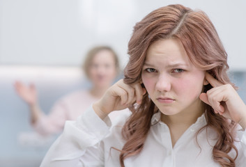 Problems between generations concept. Teen closed her ears with her hands while her mom yells at her.