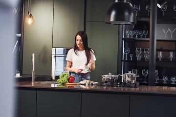 Vegetables and milk on table. Preparing food. Young beautiful brunette in casual clothes indoors in kitchen at daytime
