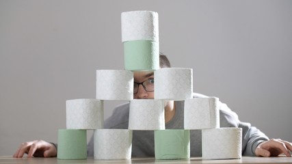 Man builds a tower of rolls toilet paper. Attractive man sits near toilet paper. Coronavirus or COVID-19. Pandemic worldwide, panic.