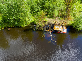 A rusty car frame in wild forest lake near the shore on summer day