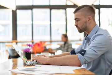 Portrait of young businessman working on laptop while sitting at office desk. Young businessman working with laptop while sitting in modern office,