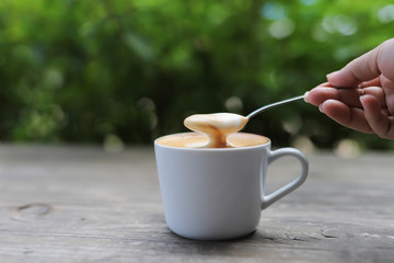 Hand holding a spoon that scoop the coffee in a cup. Cup of Cappuccino coffee with a delicious crema.
