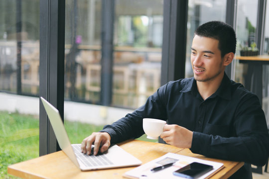 Portrait Of A Young Business Man Using Laptop Computer While Working. Young Asian Business Men Working With Laptop In Coffee Shop Cafe.