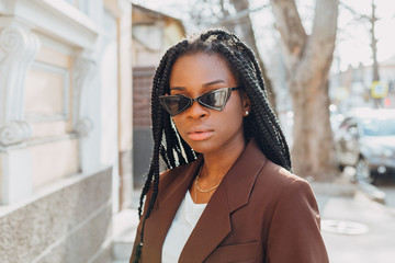 Close up portrait of a beautiful young african american woman with pigtails hairstyle in a brown business suit walks along spring streets