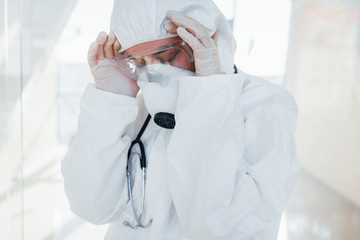 Feels bad and sick. Female doctor scientist in lab coat, defensive eyewear and mask standing indoors
