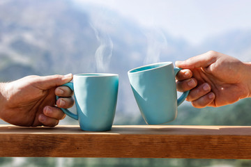 man hands with mugs of hot drink and blurred landscape of mountains. 