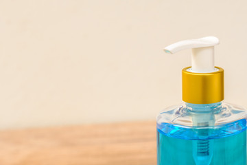 Alcohol gel in a pump bottle placed on a wooden floor beside a white wall.