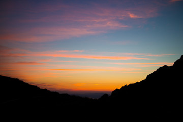 Bright pink-orange sunset sky on a black silhouette of mountains