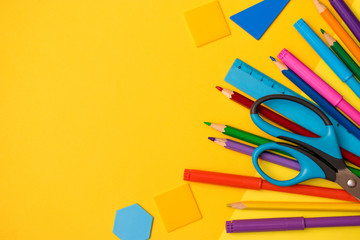 Back to school concept flat lay.Color pencils,felt pens,ruler,scissors and plastic geometric shapes on the yellow background.Copy space for text,top view