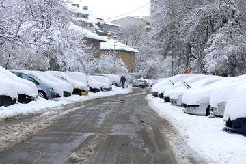 Uncleaned streets with heavy snowdrifts after snowfall in the city, cars under the snow.