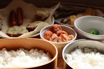 ご飯をつめた弁当箱と梅干しと他のおかず