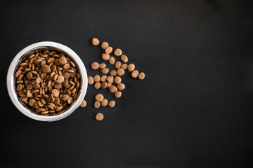 Dry cat food in a silver round dish on a black background. Flat lay, top view, copy space