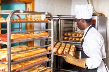 Worker of bakery putting baked baguettes on tray rack