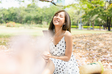 Young Asian women are relaxing on summer holidays by listening to music on their smartphone headphones in park.