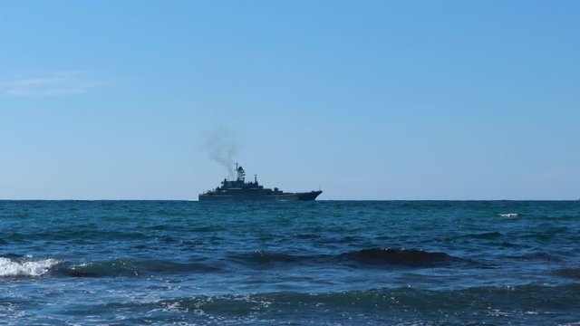 A combat military cruiser sails along the sea coastal zone against the blue sky.