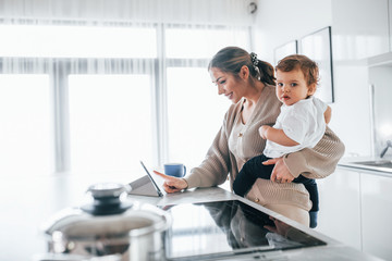 Female blogger mother with her kid together indoors at home at weekend using tablet