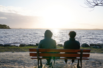 two teenager sitting at bench watching the sunset over the sea lake in solitude