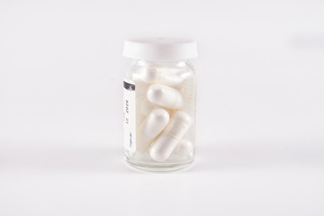 Glass pill bottle full with white capsules (frog eye view on white background)