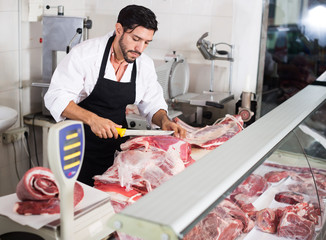 Handsome butcher is cutting meat for clients