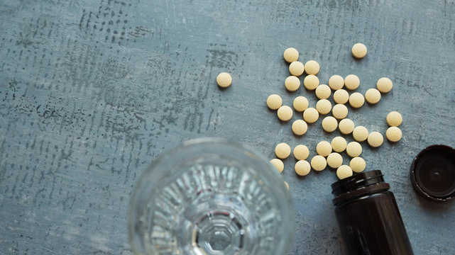 yellow round tablets or pills vitamins flat lay on blue stone concrete table with black plastic bottle and glass cup, top-down view, copy space, horizontal stock photo image still life background