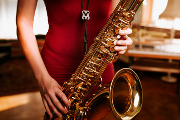 Young beautiful woman smile while playing tenor saxophone in nice cozy condo flat in the sundown with a sythesizer in the background