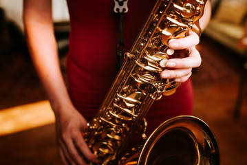 Young beautiful woman smile while playing tenor saxophone in nice cozy condo flat in the sundown...