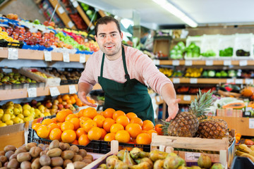 Young man in apron selling fresh oranges and fruits on the supermarket