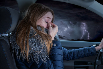 Woman driving overtired car during thunderstorm and rubbing her eyes