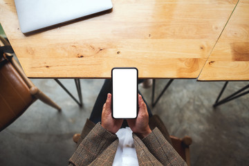 Top view mockup image of a woman holding mobile phone with blank white desktop screen with laptop on table
