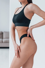 Slender woman in black fitness underwear standing indoors in room at daytime