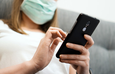 Woman in medical mask using mobile phone. Isolation at home.