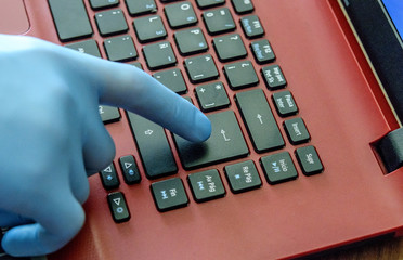Hand of young man in medical glove on the laptop key. Working and learning online in period of qaurantine. Stay safe concept.